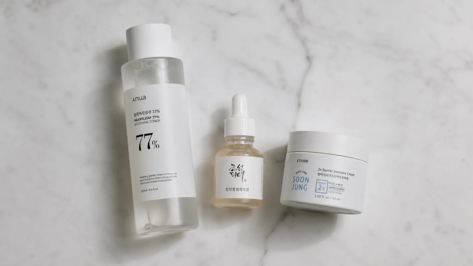Flatlay of a simplified skincare routine on a white marble surface: toner, one serum, and the Anua PDRN cream jar