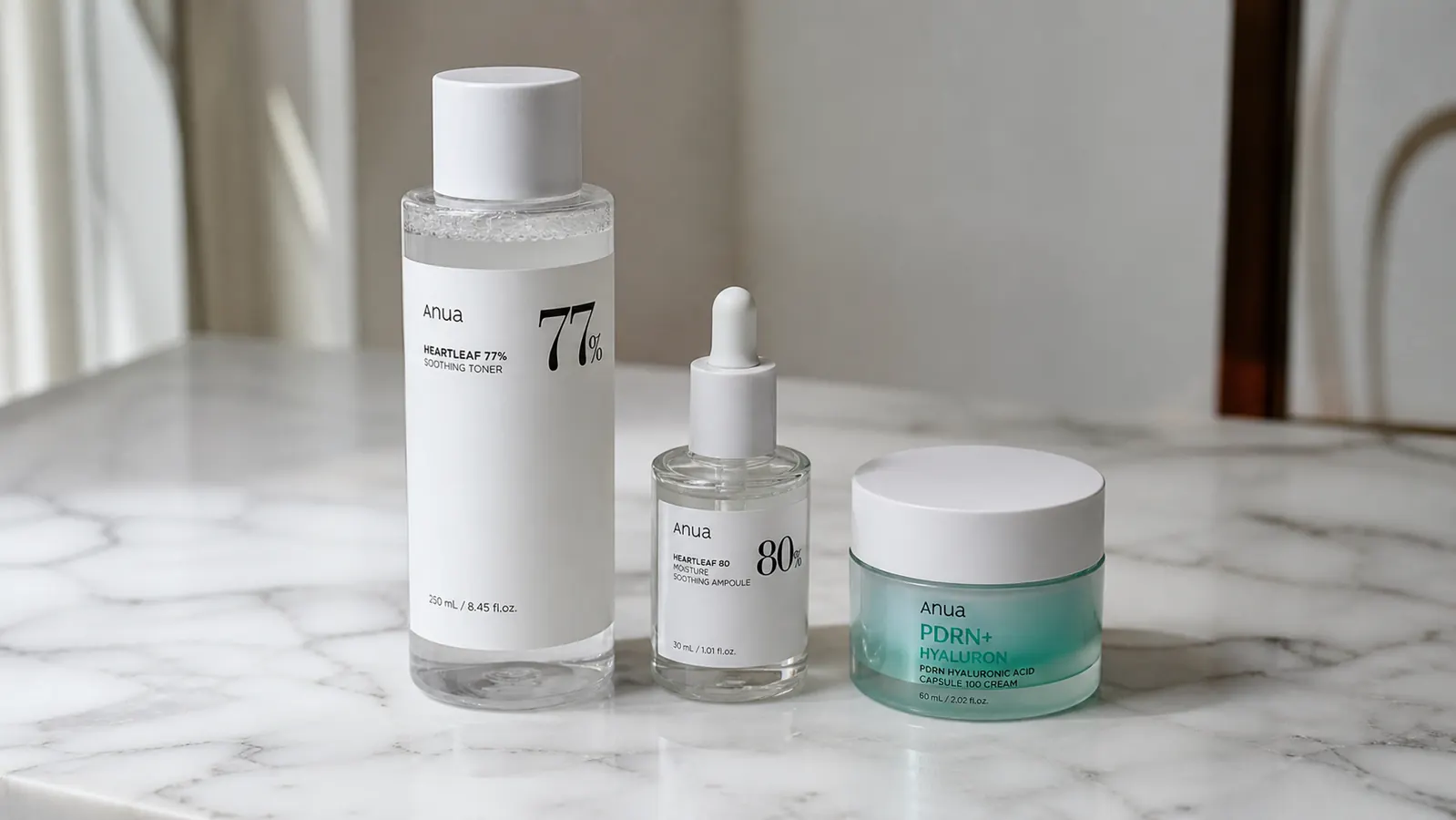 Flatlay of Anua PDRN cream jar alongside a toner bottle and a serum dropper on a white surface, showing a minimal K-beauty routine