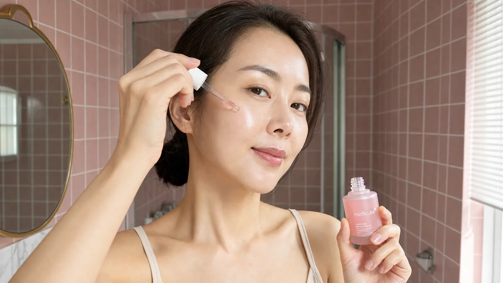 Woman applying a serum to her cheek with fingertips, skin looking smooth and dewy in warm light