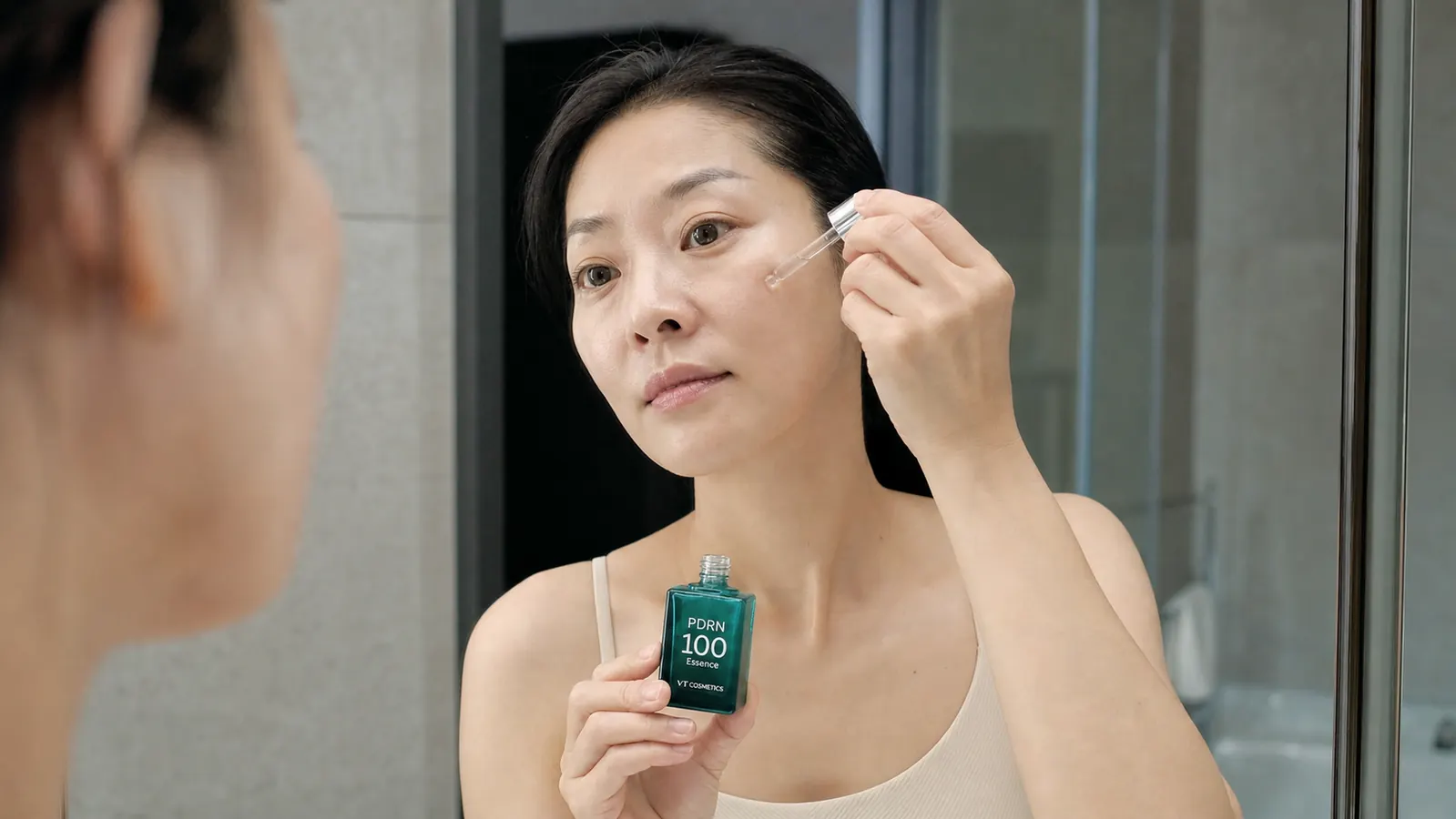 Hand pressing a dropper of VT PDRN 100 Essence onto fingertips before applying to cheek