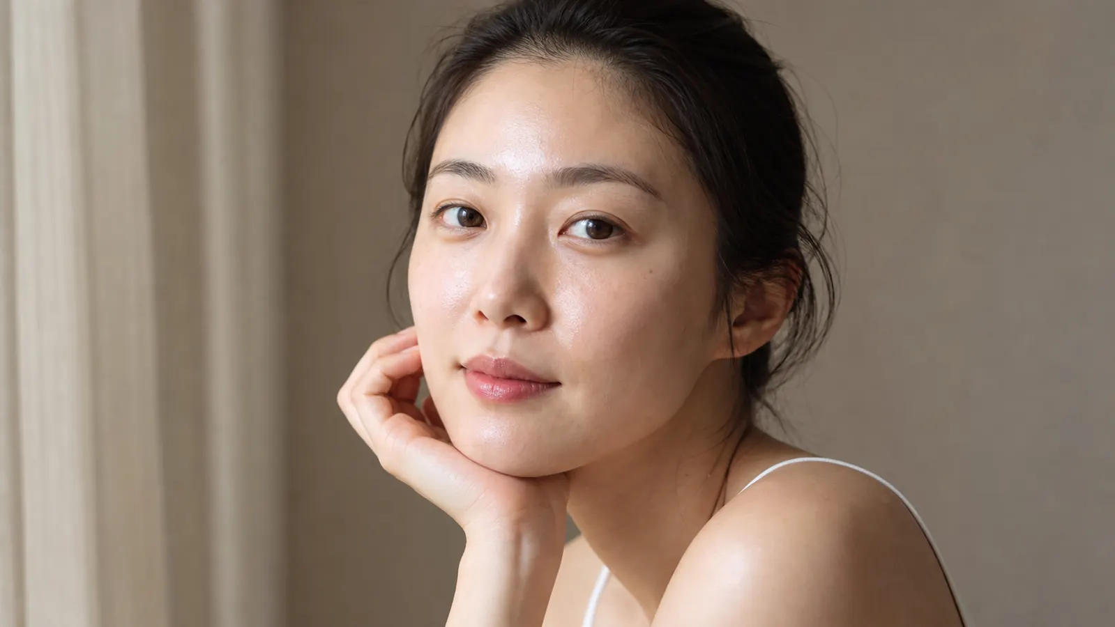 Close-up of a woman with luminous, dewy skin looking toward natural window light